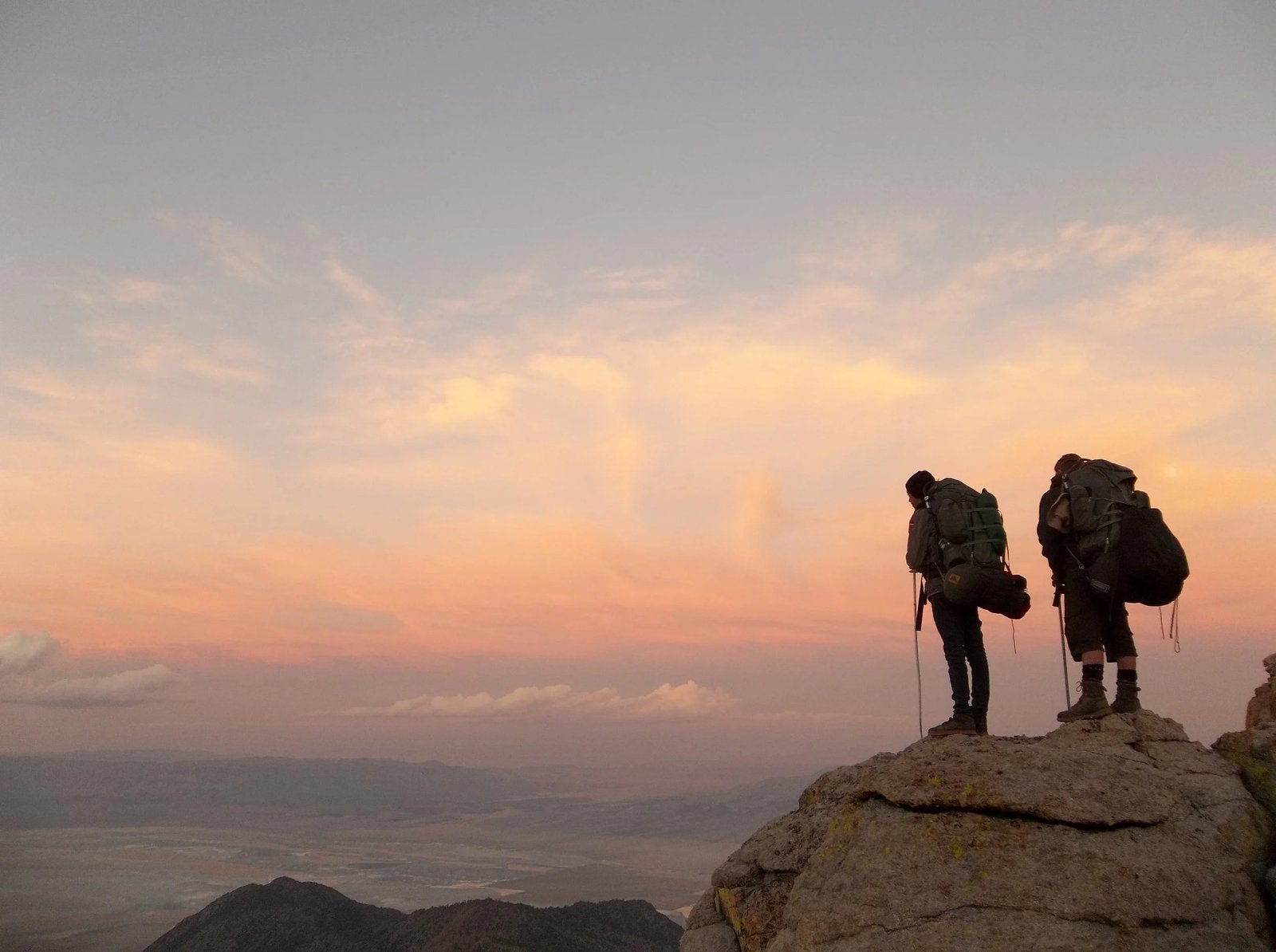Two backpackers standing on a mountain overlook at sunset
